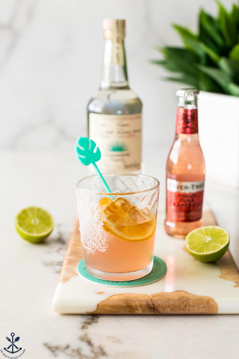 A cocktail with a bottle of tequila in the background and a bottle of soda off to the side