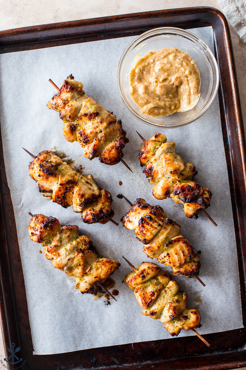 Overhead photo of six cooked chicken skewers and a bowl of honey lime butter