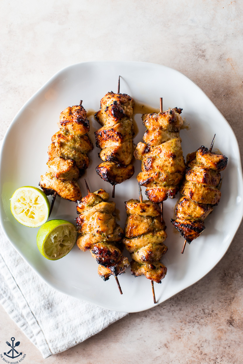 Overhead photo of a plate of chicken skewers with two lime halves