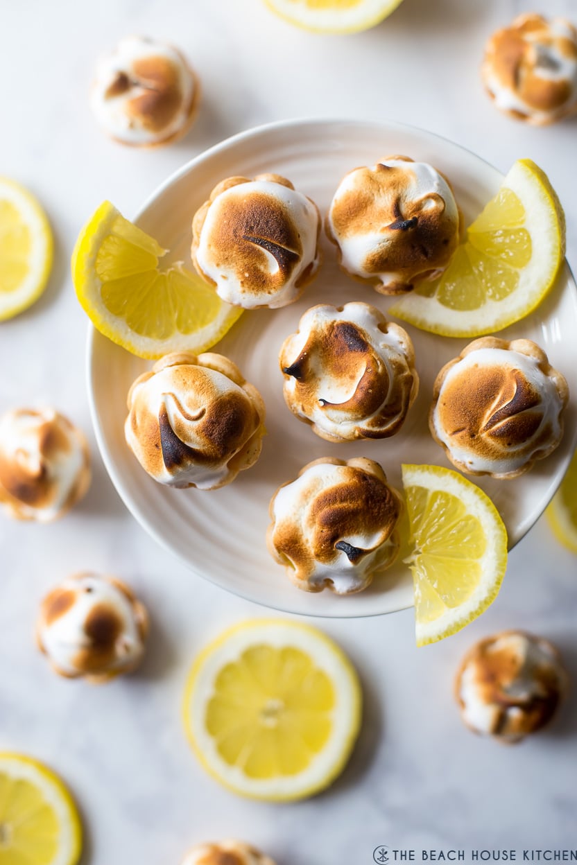 Overhead photo of mini lemon meringue pies on a small cake plate with lemon slices