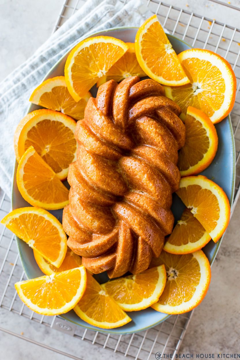 Up close overhead photo of an orange loaf cake on a plate surrounded by orange slices