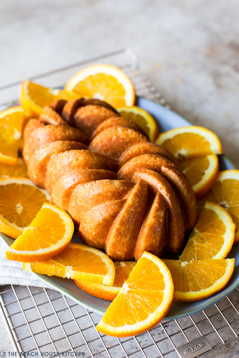 An orange loaf cake on a plate surrounded by orange slices