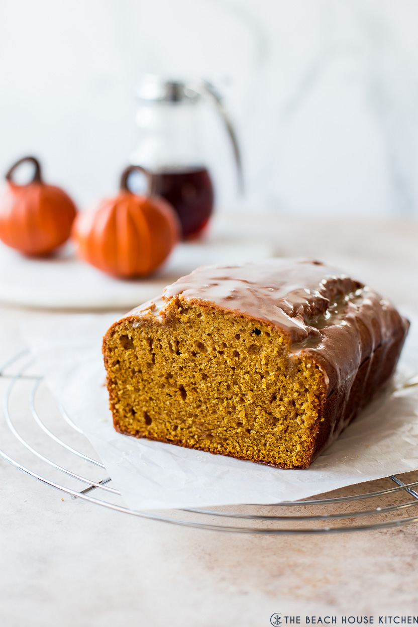 A loaf of pumpkin bread glazed with a maple glaze on a wire rack