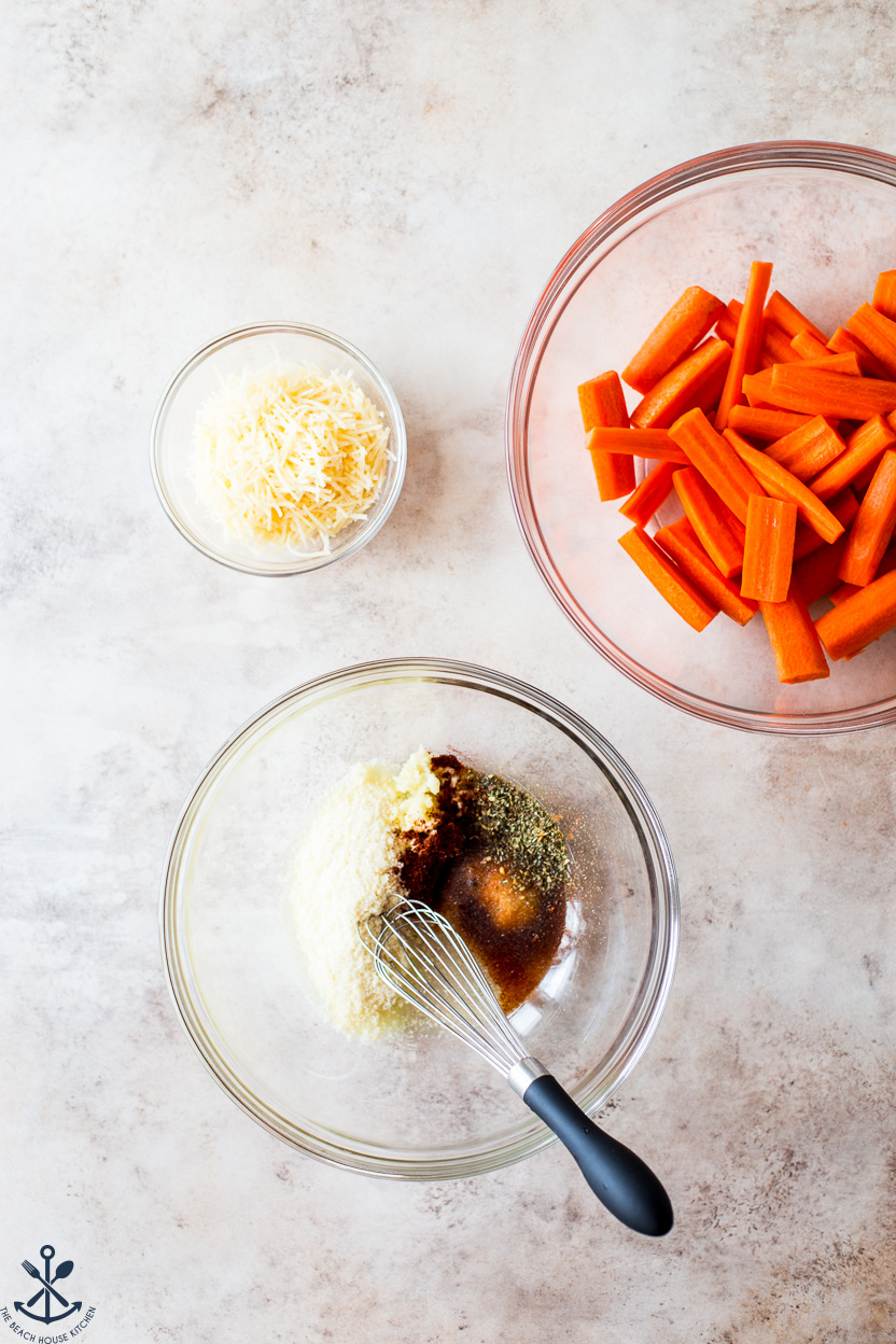 Overhead photo of a bowl full of coating for parmesan carrots, a bowl of sliced carrots and a bowl of shredded parmesan