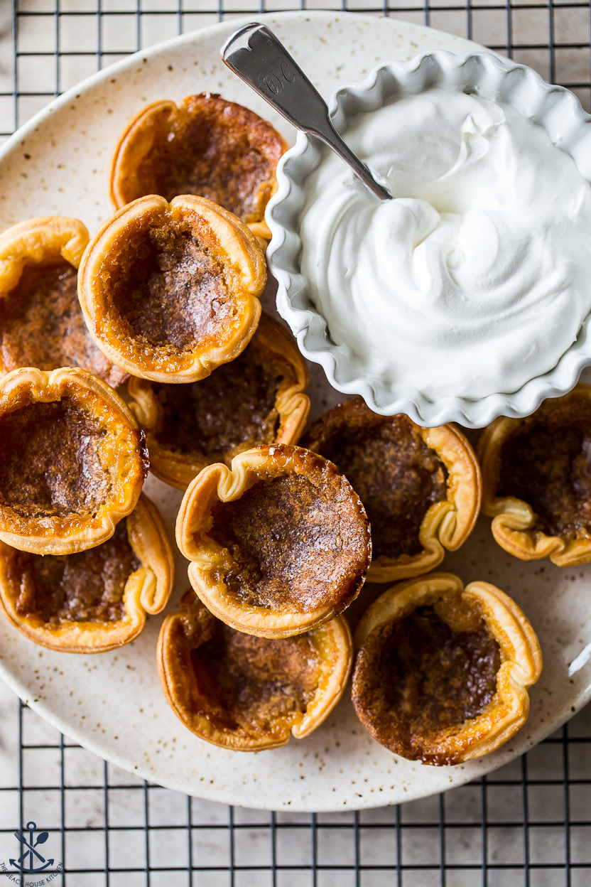 Up close overhead photo of a plate of butter tarts with a bowl of whipped cream