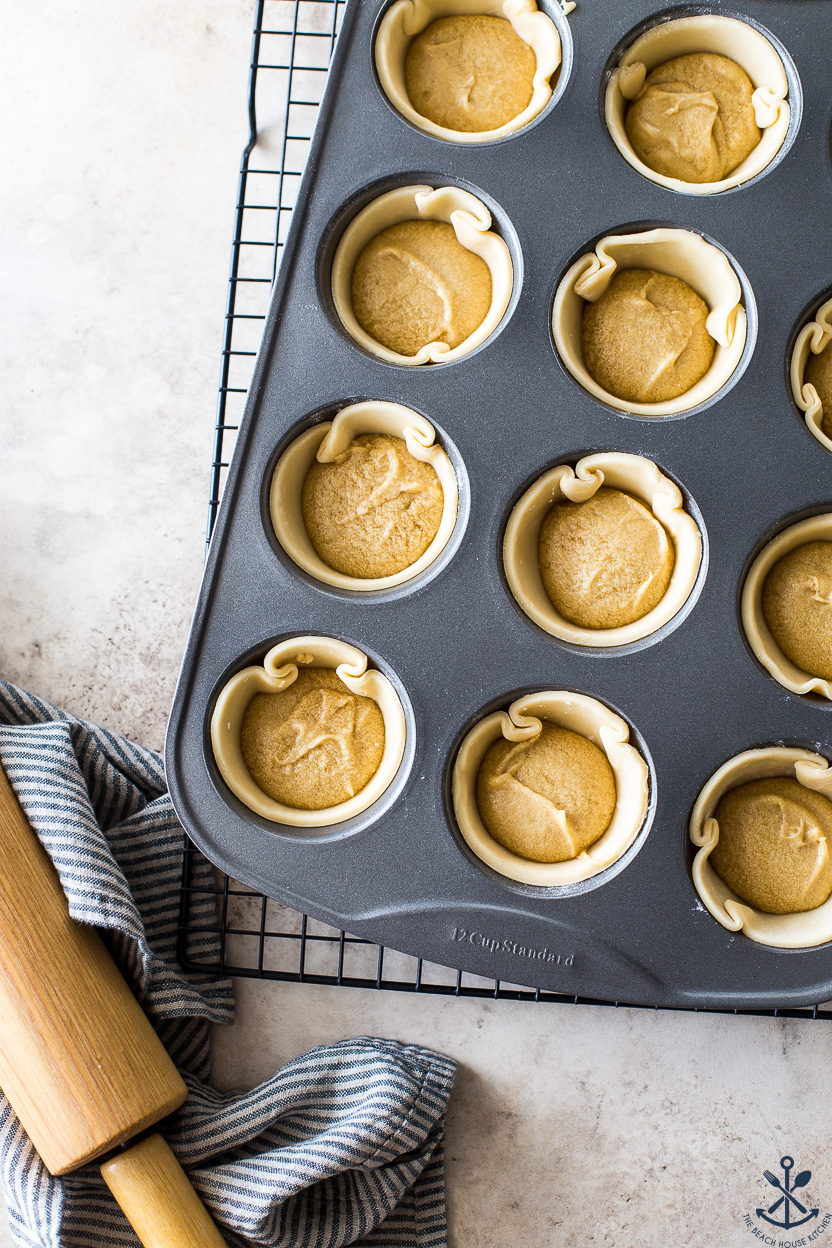 Overhead photo of pre-baked butter tarts in a muffin pan on a wire rack