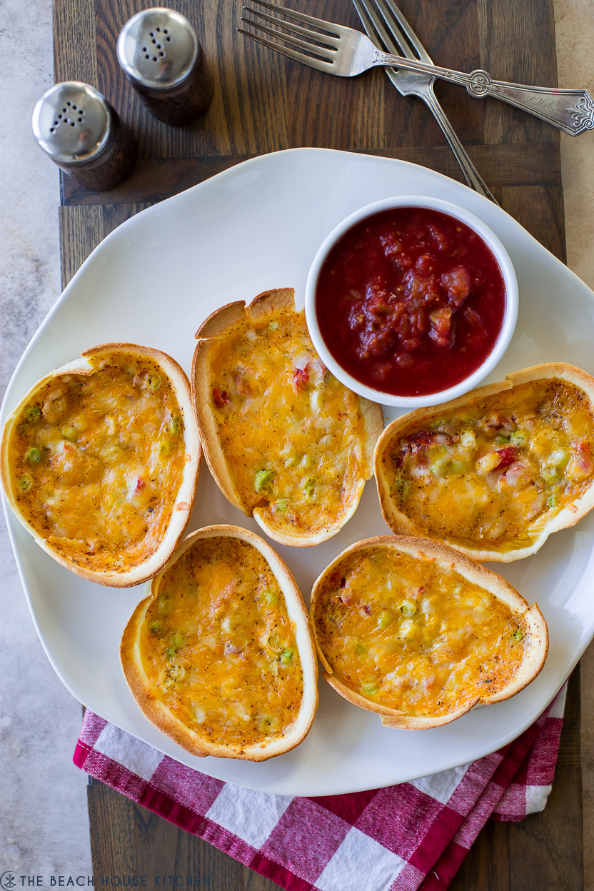 Overhead photo of 5 taco boat quiches on a white plate with a bowl of salsa