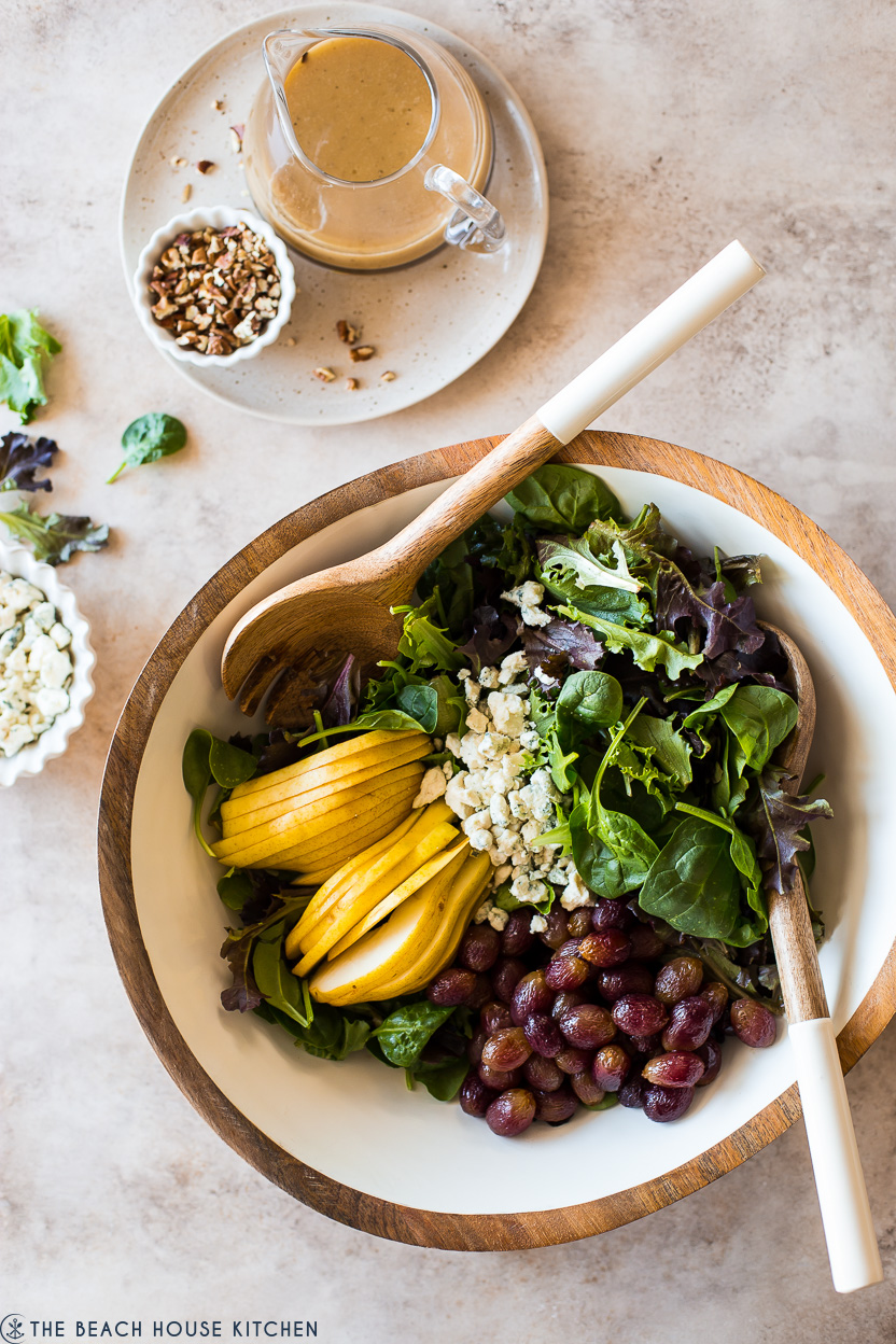 Overhead photo of a salad bowl filled with greens, pears, roasted grapes and blue cheese crumbles