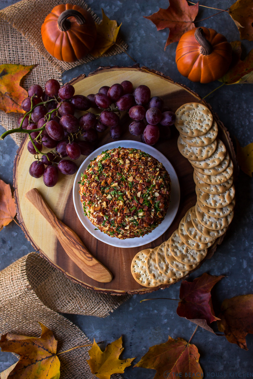 Overhead photo of a cheese ball on a wooden platter with crackers and grapes