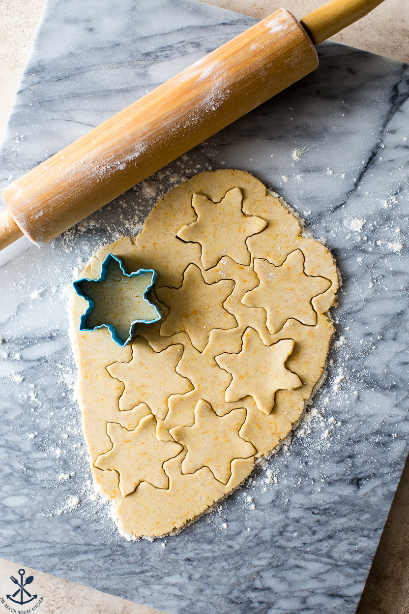 Overhead photo of snowflake cookie cutouts on a marble board with a rolling pin