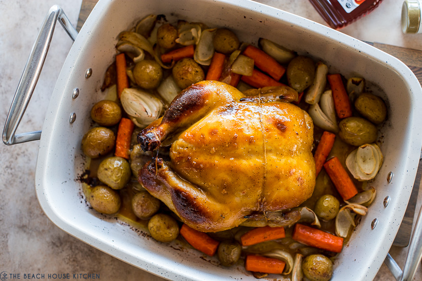 Overhead photo of a roast chicken and veggies in a white roasting pan