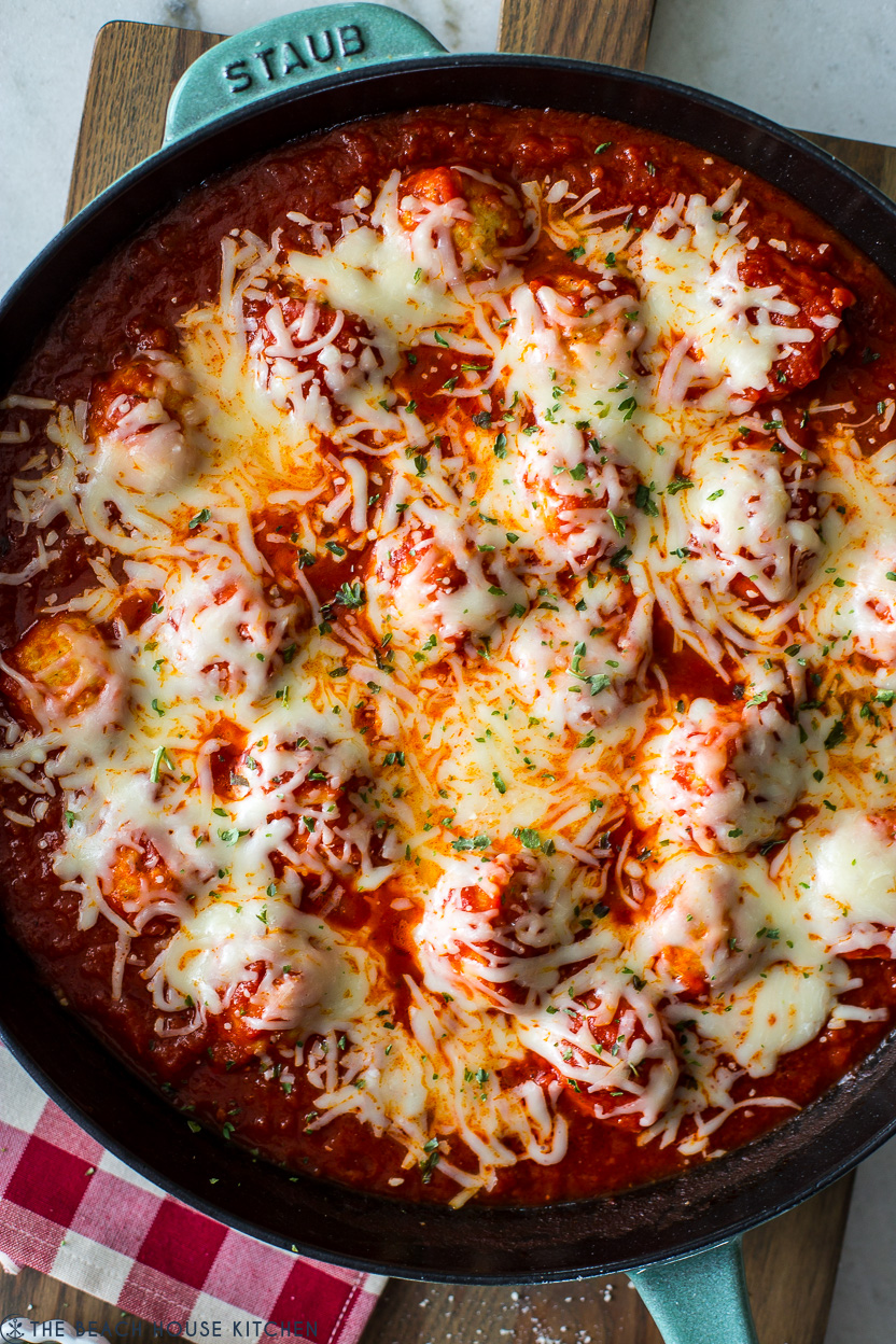 Up close overhead photo of a skillet of meatballs and sauce topped with cheese