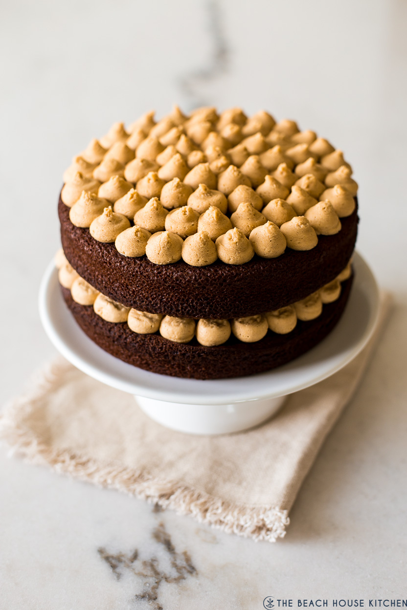 A photo of a chocolate cake with peanut butter piped frosting on a white cake pedestal