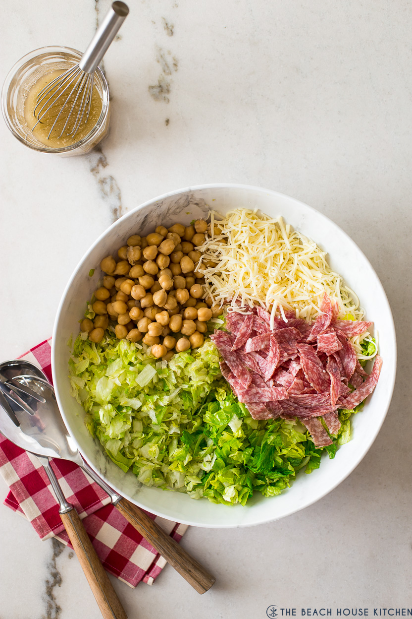 Overhead photo of pre-mixed chopped salad with greens, chick peas, salami and shredded cheese.