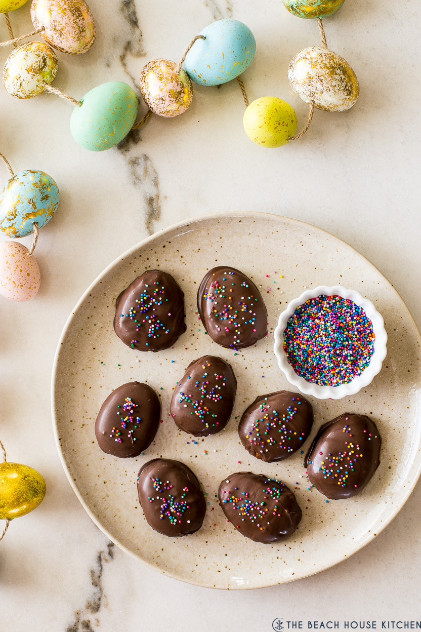 Overhead photo of a plate of chocolate covered peanut butter eggs with colored eggs around the plate