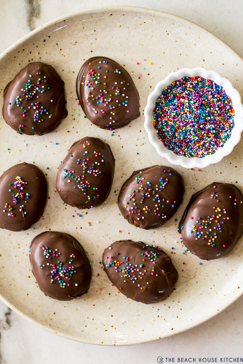Up close overhead photo of a plate of homemade peanut butter eggs with a small bowl of nonpareils