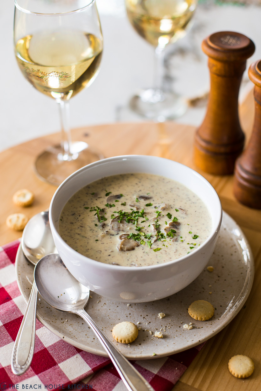 A bowl of classic cream of mushroom soup on a plate with spoons and crackers