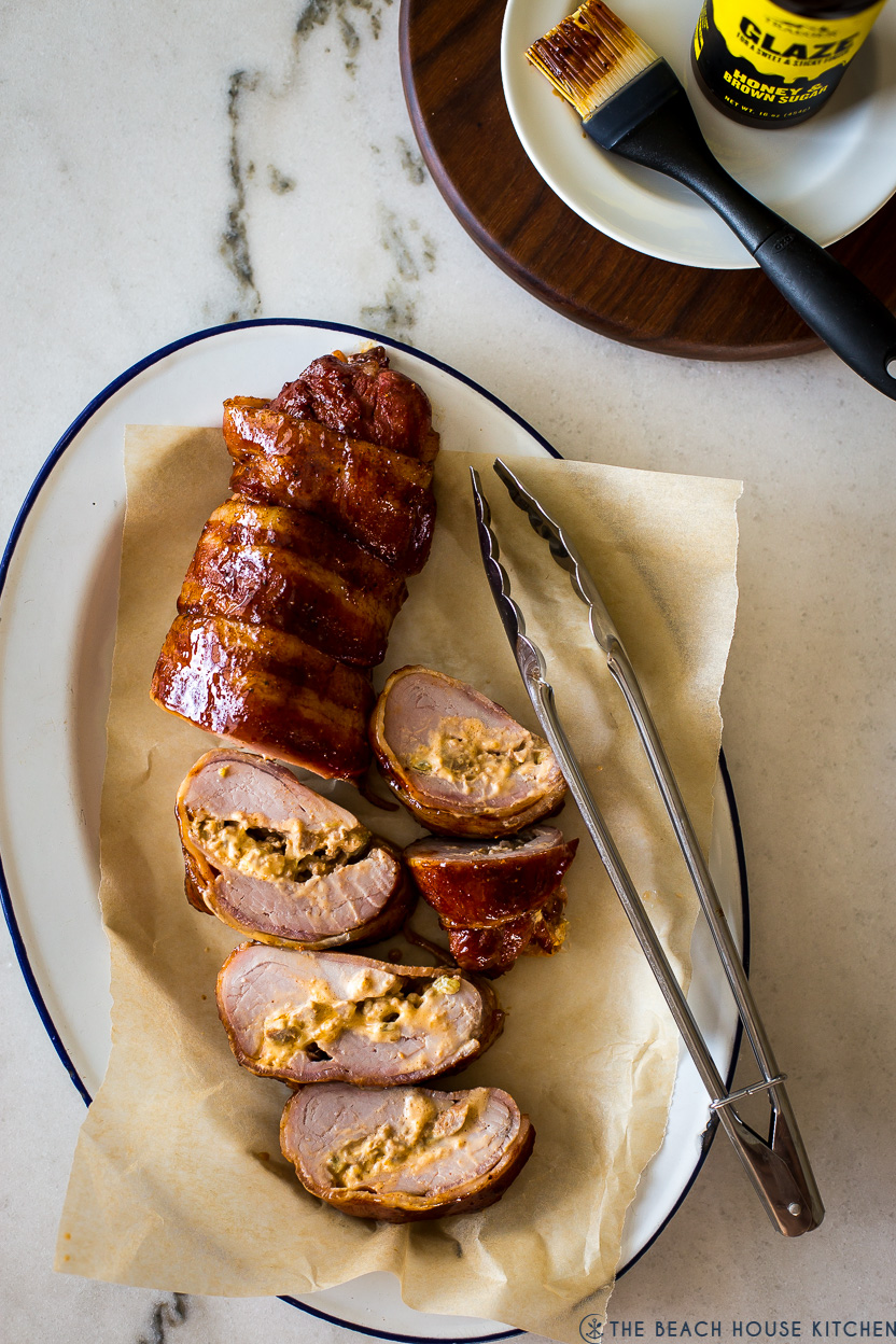 Overhead photo of a stuffed bacon wrapped pork tenderloin on an oval platter