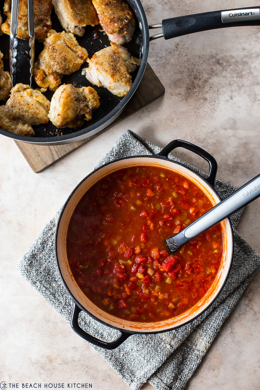 Overhead photo of a Dutch oven filled with a rich tomato sauce and a skillet of cooked chicken thighs