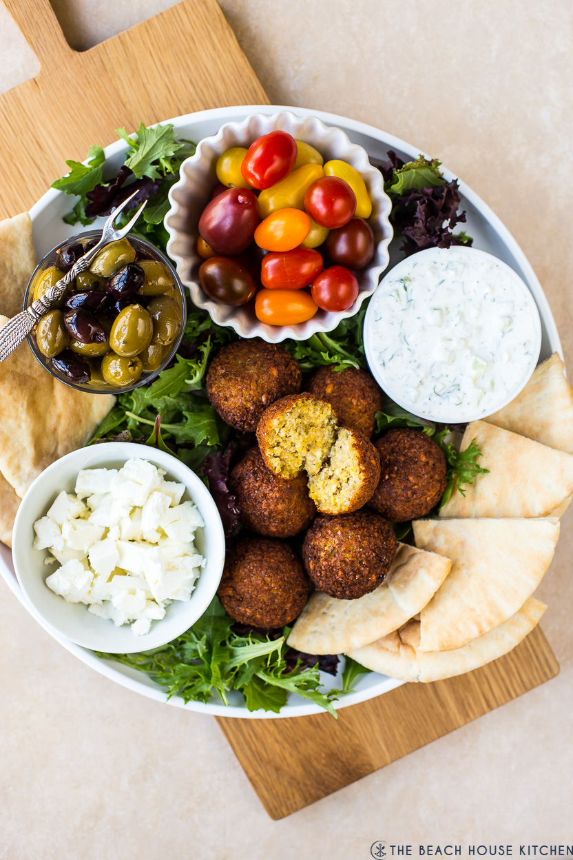 Overhead photo of a falafel platter with tzatziki sauce, tomatoes, feta, pita and olives