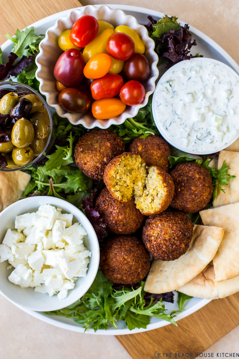 Up close overhead photo of a falafel platter with tzatziki sauce, tomatoes, feta, pita and olives