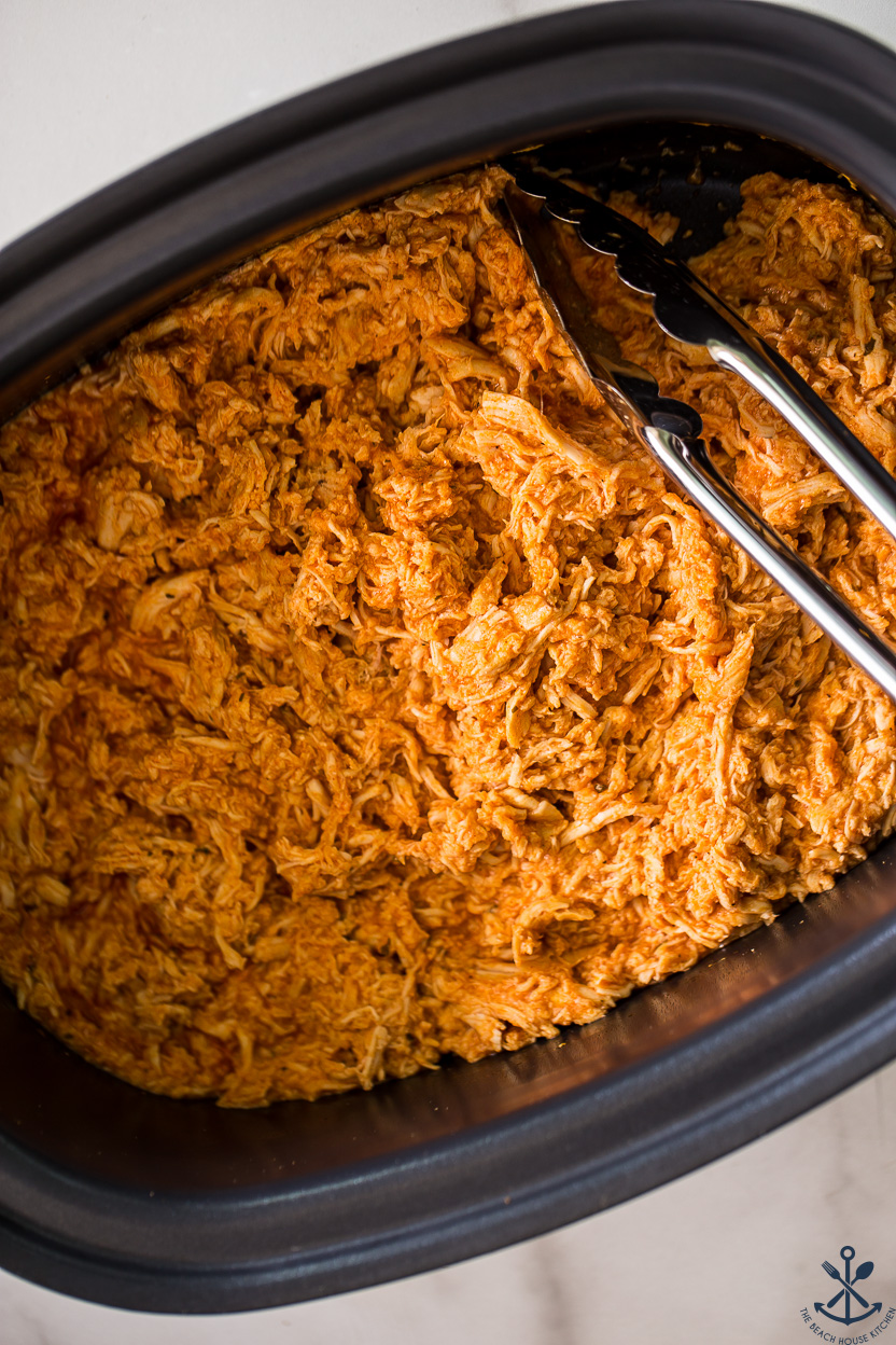 Up close overhead photo of a slow cooker of shredded buffalo chicken