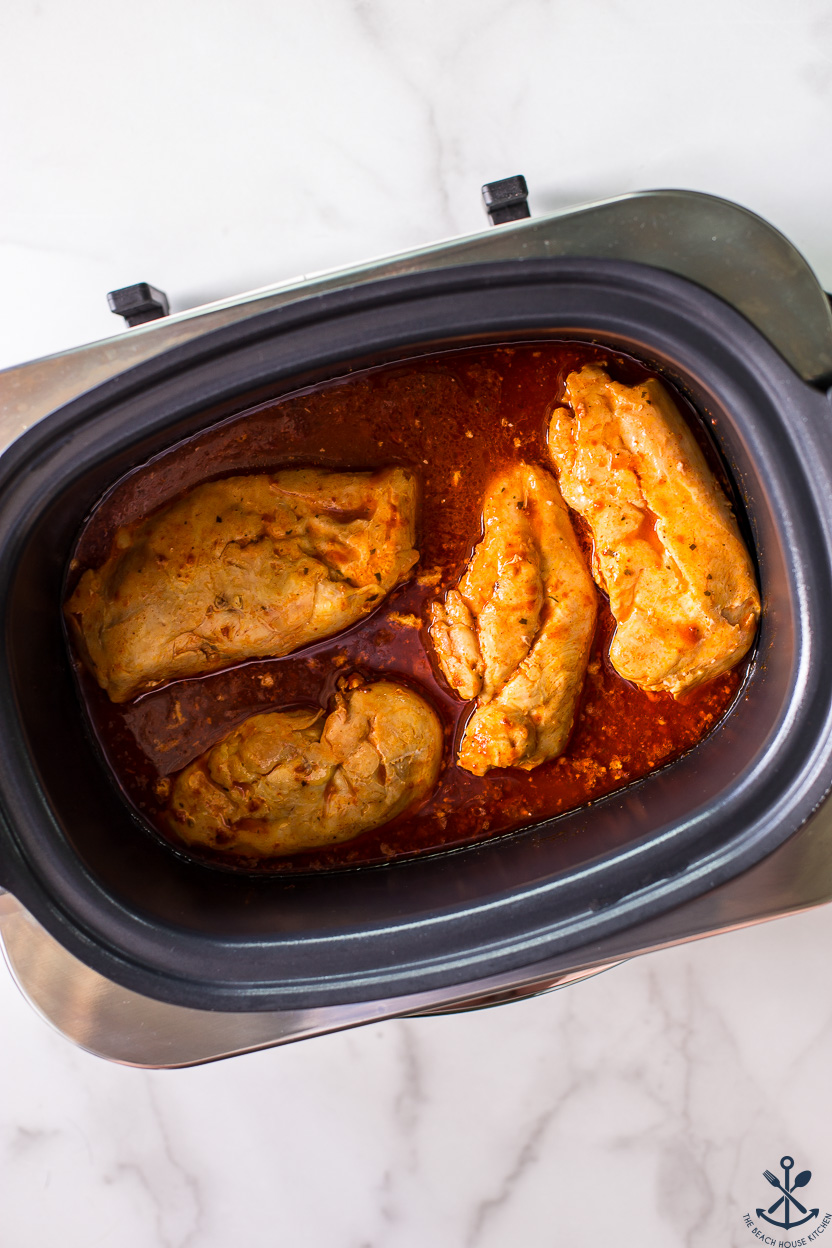 Overhead photo of a slow cooker with cooked chicken breasts