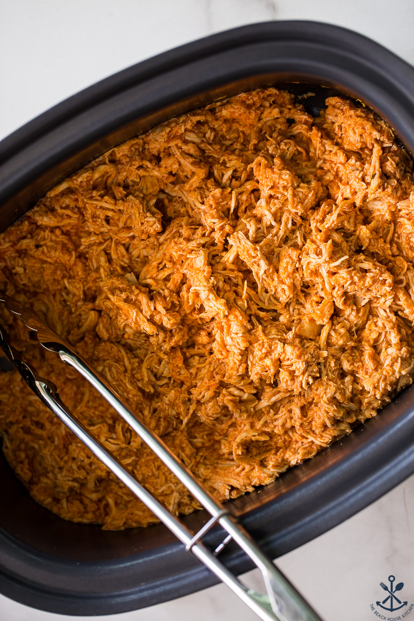 Up close overhead photo of a slow cooker of shredded buffalo chicken