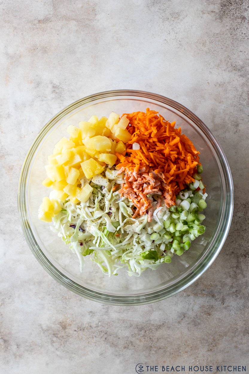 Overhead photo of a glass bowl of pre-mixed pineapple coleslaw ingredients