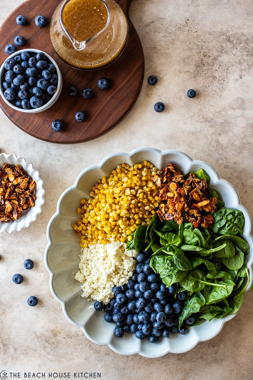Overhead photo of a serving dish of corn, spinach leaves, blueberries, cotija cheese and candied almonds