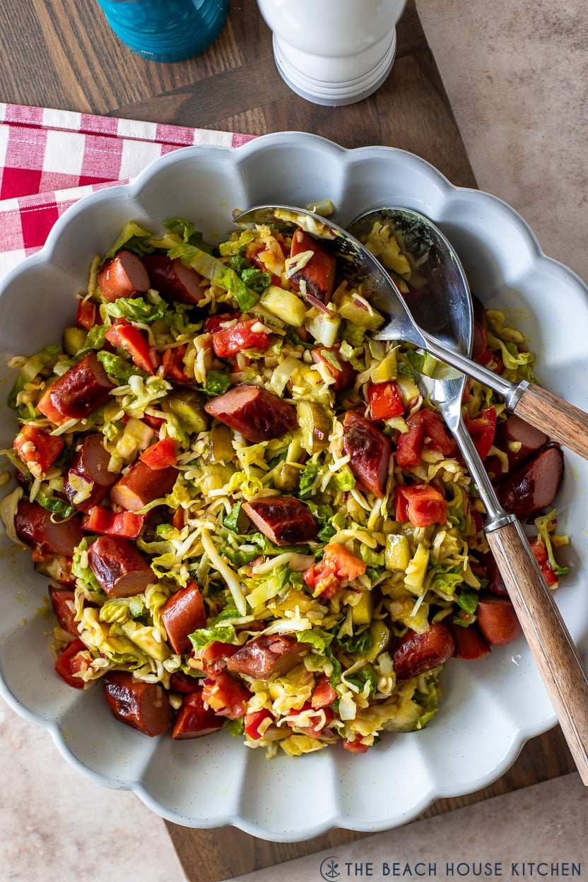 Up close overhead photo of a white scalloped serving dish filled with a hot dog salad