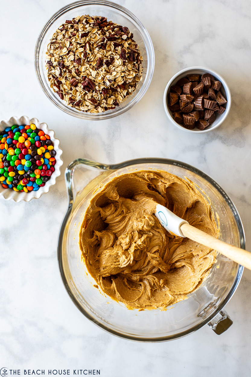 Overhead photo of a bowl of cookie dough, a bowl of M&M's, a bowl of peanut butter cups and a bowl of oats and pecans
