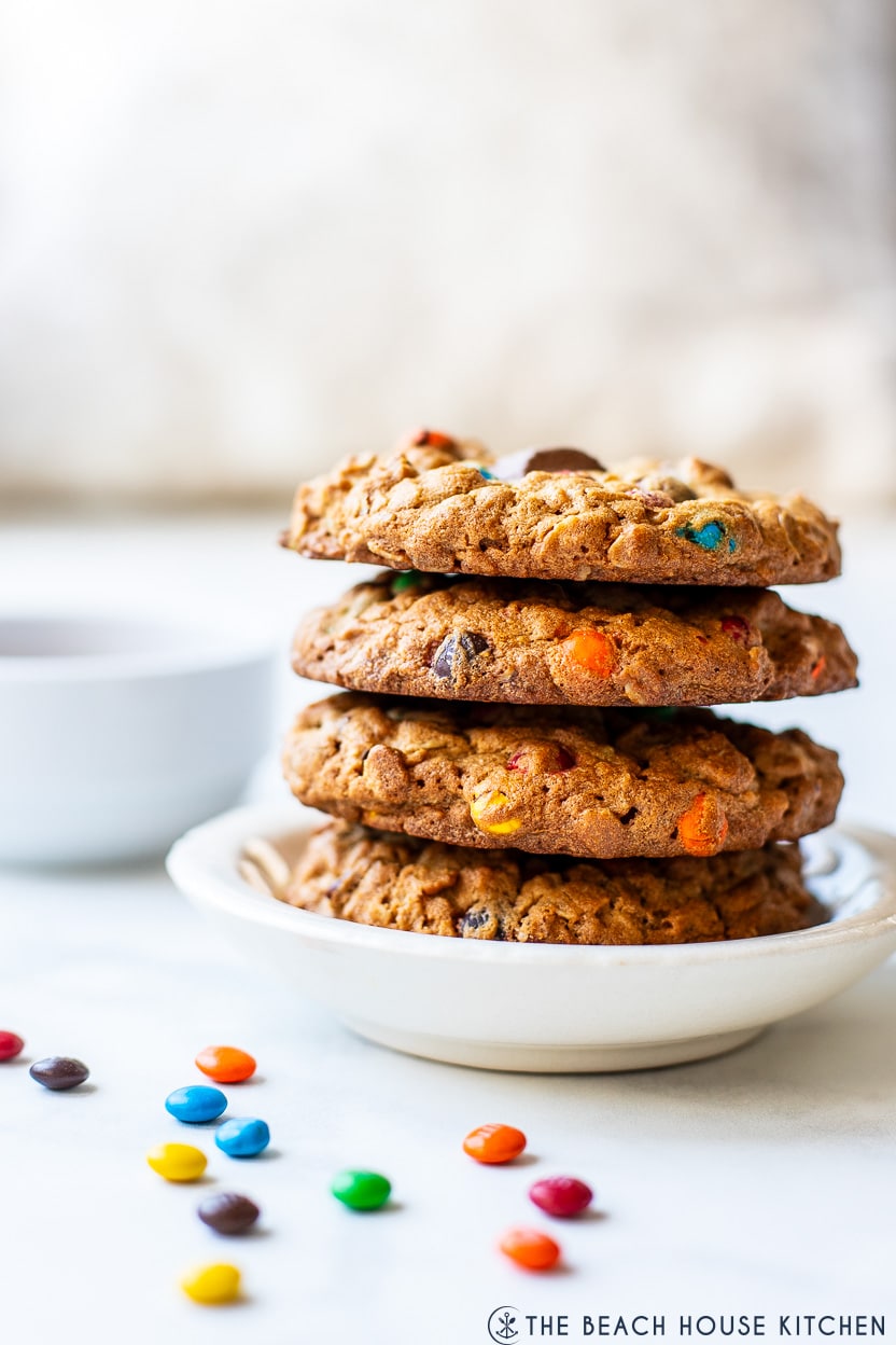 A stack of four Oatmeal Peanut Butter Chocolate Candy Cookies on a small white plate surrounded by mini M&M's