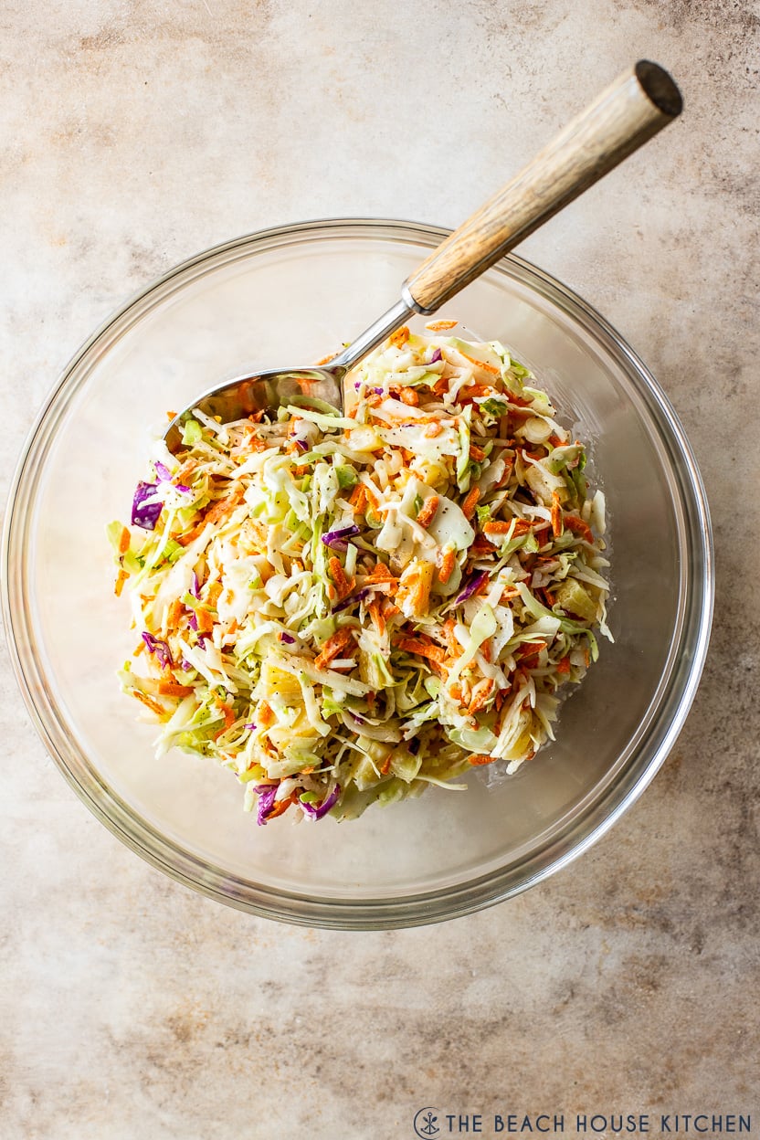 Overhead photo of a glass bowl of pineapple coleslaw with a spoon in it