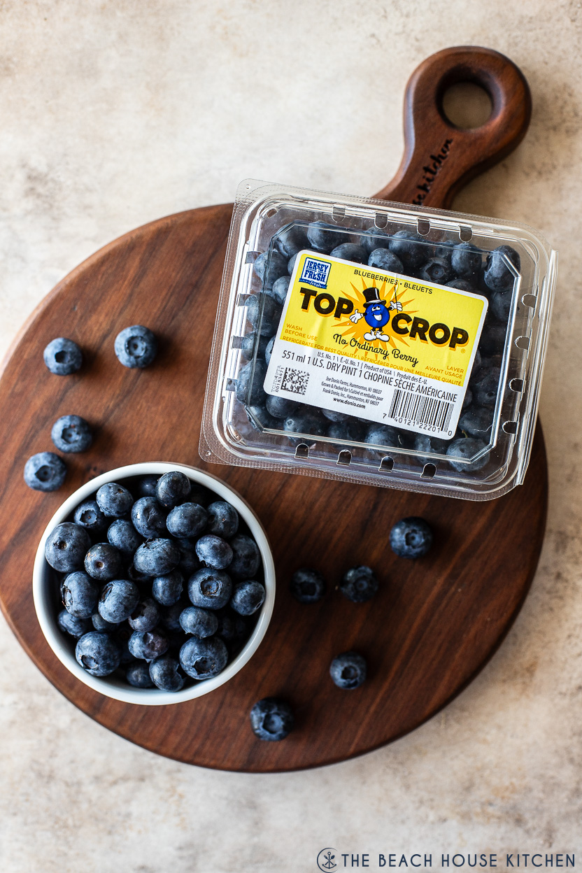 Overhead photo of a container of blueberries and a small bowl of blueberries on a round wooden board