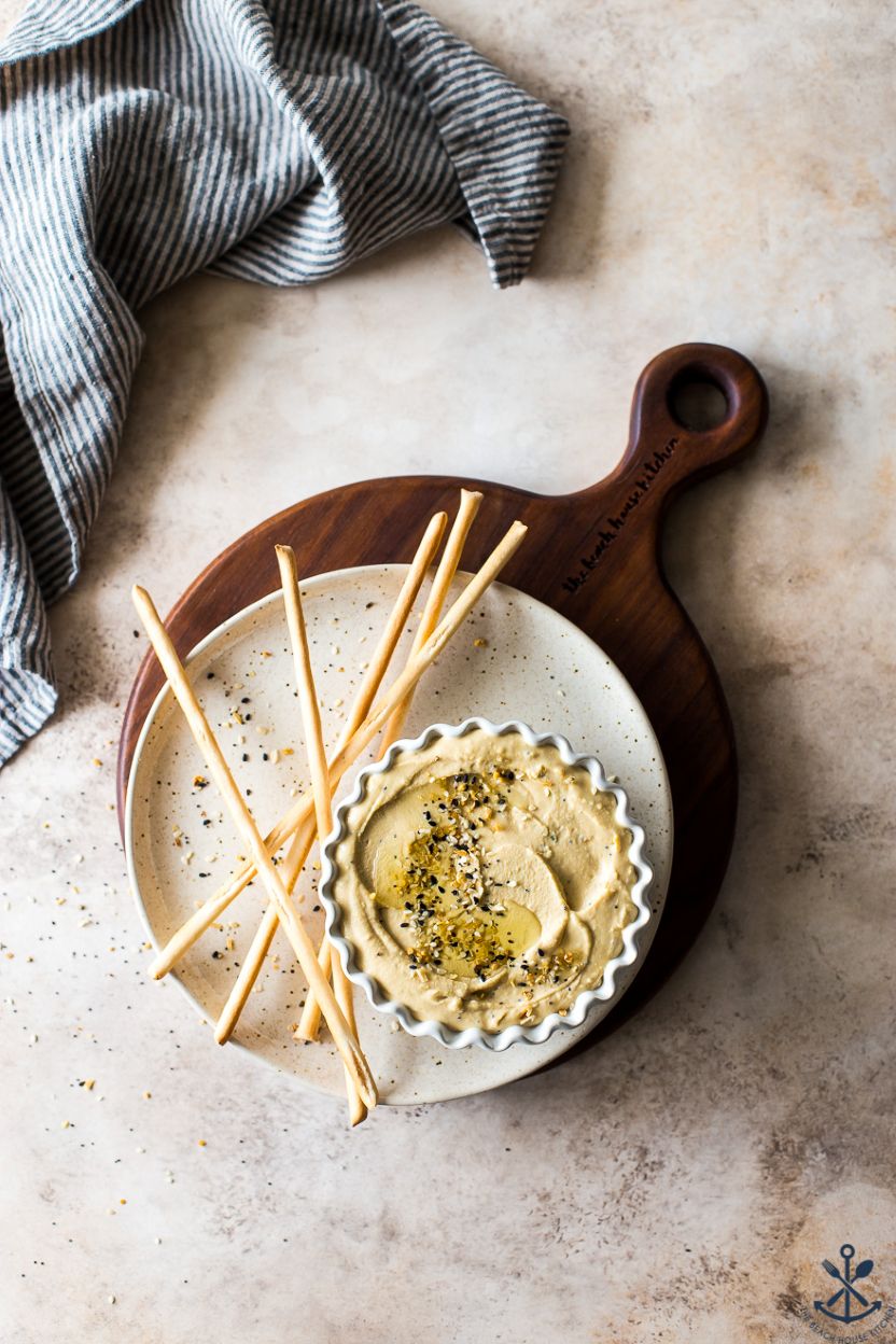 Overhead photo of a dish of hummus on a plate with thin breadsticks