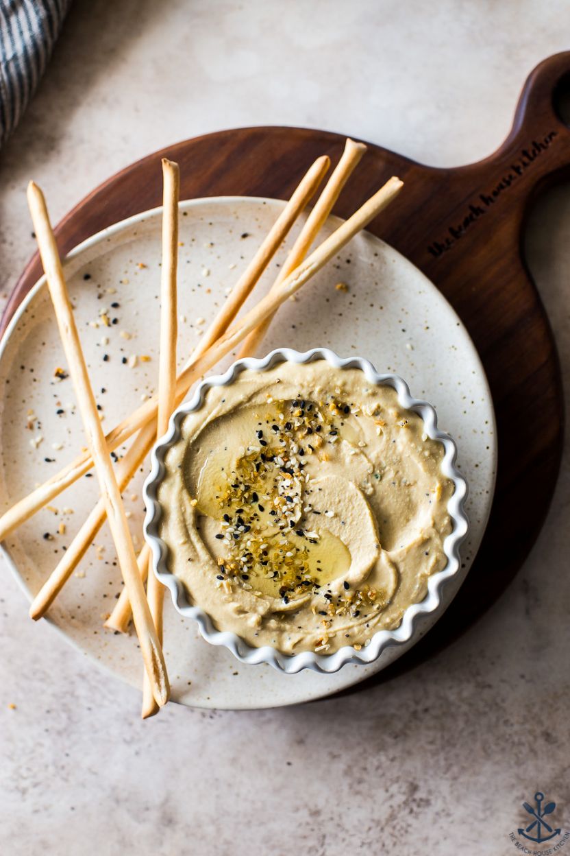Up close overhead photo of everything hummus in a bowl on a plate with thin breadsticks