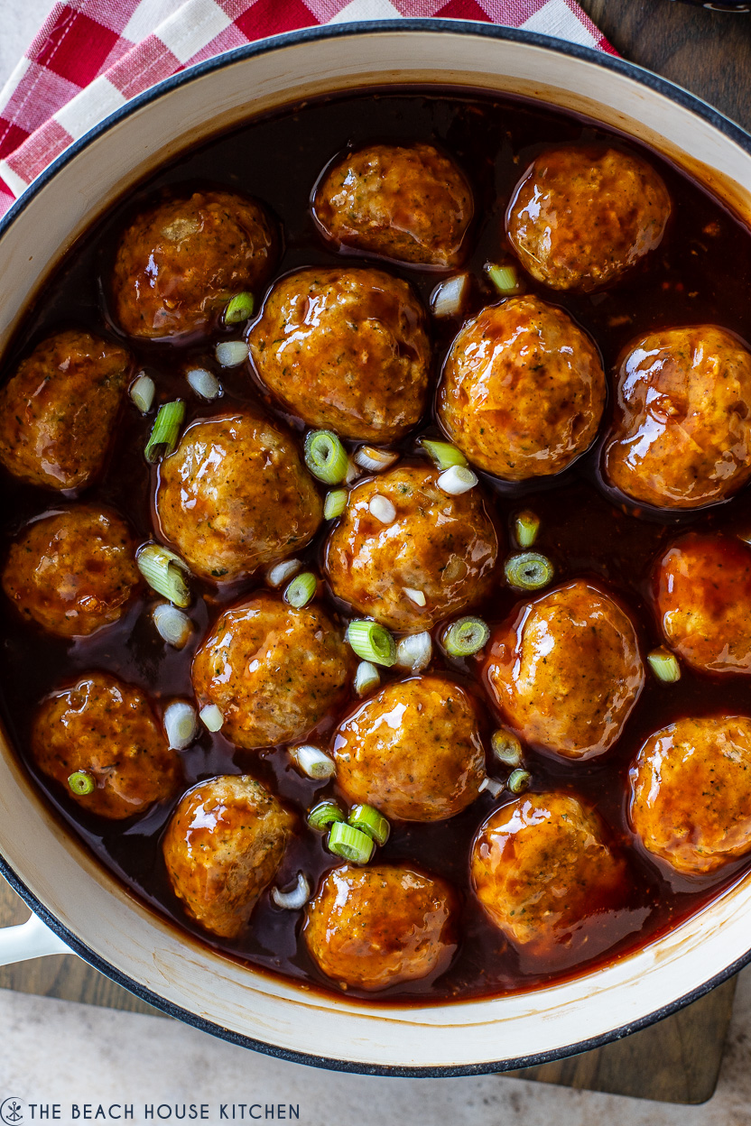 Super up close photo of a skillet of huli huli chicken meatballs topped with sliced green onions