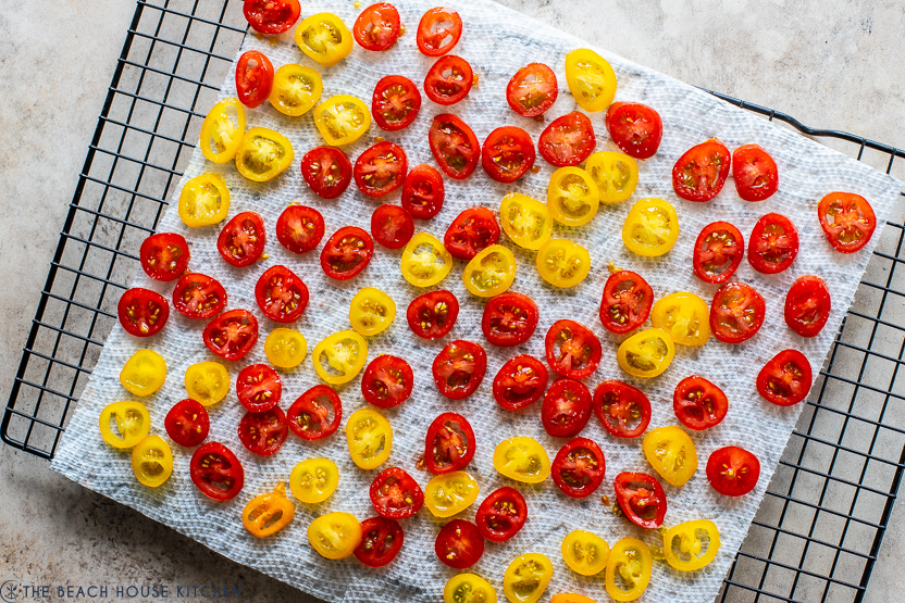 Overhead photo of mini tomato slices on a paper towel on a wire rack
