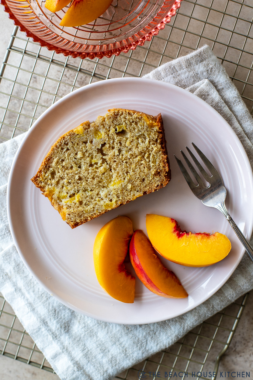 Up close overhead photo of a slice of peach bread on a plate with a few fresh peach slices