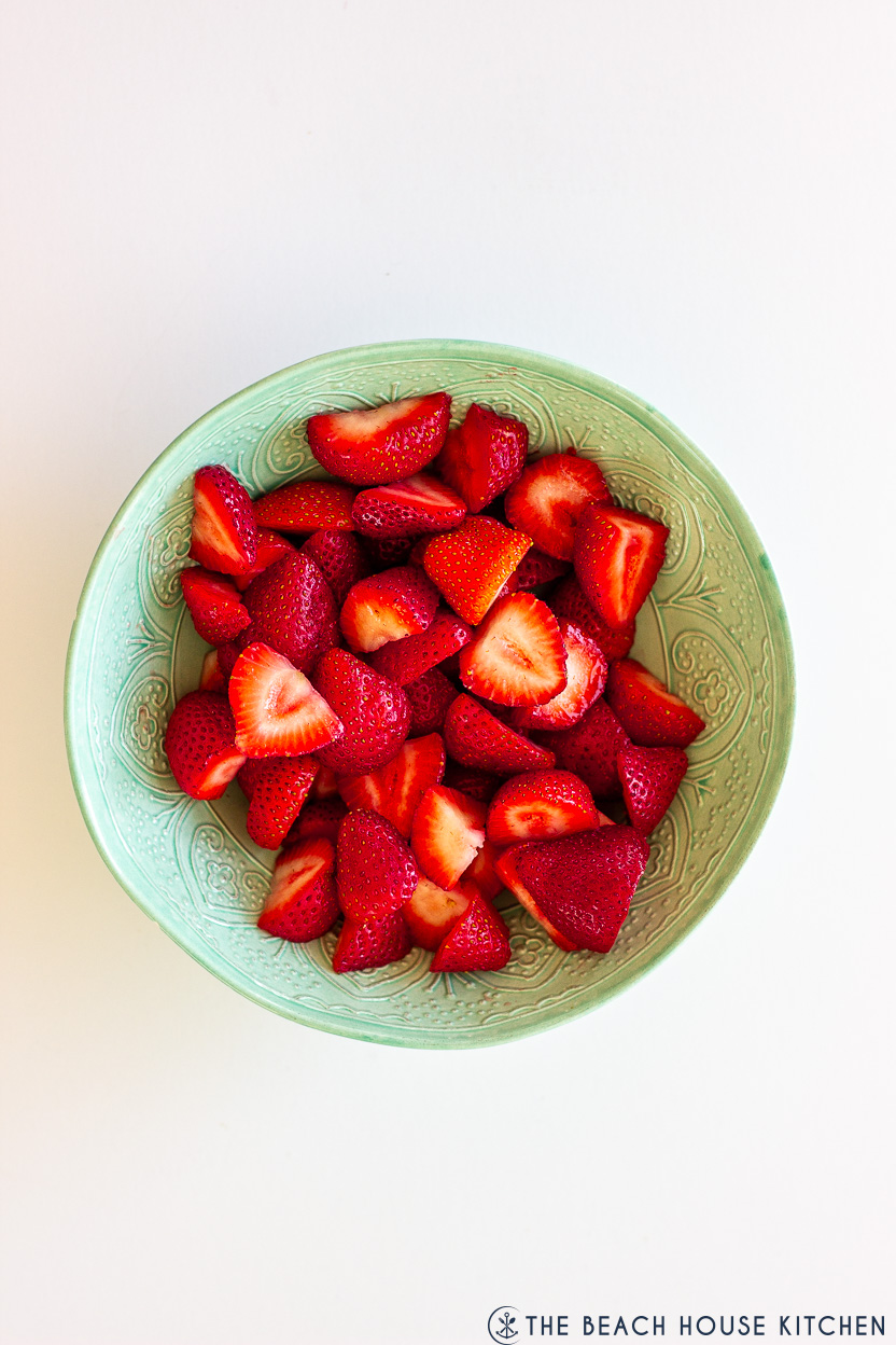Overhead photo of a pale green bowl of fresh sliced strawberries