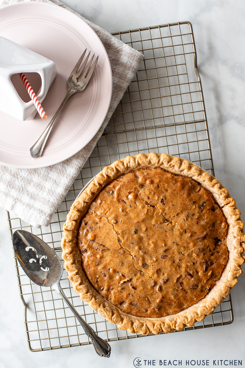 Overhead photo of a chocolate chip pie on a wire rack as well as a plate with a fork and a container of milk