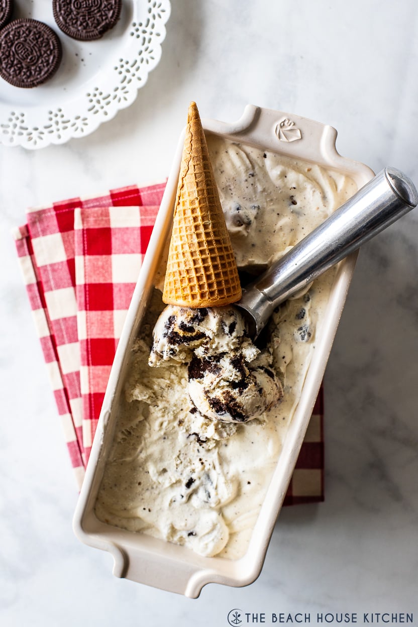 Overhead photo of a loaf dish filled with Slow churn oreo ice cream, a sugar cone and a silver scooper
