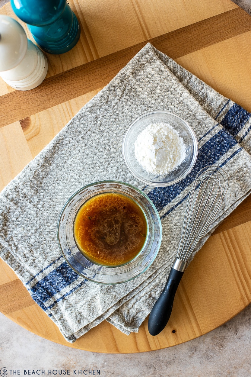 Overhead photo of a small bowl of beef gravy, a small bowl of cornstarch and a whisk