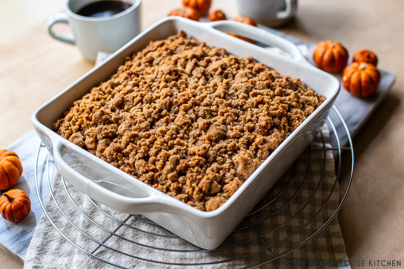 A photo of a pumpkin crumb snack cake in a white dish on a wire rack