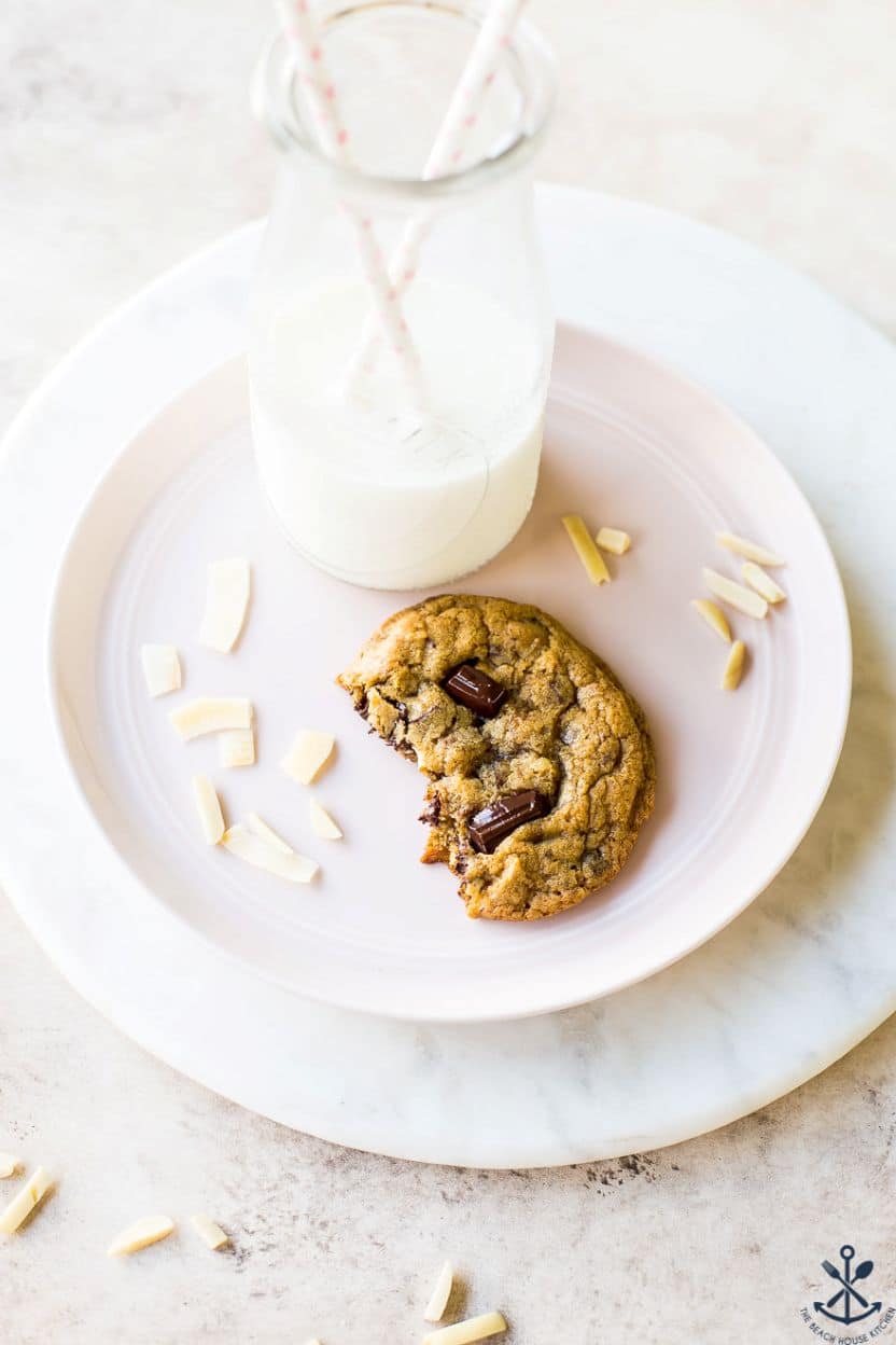 A half of a chocolate chip cookie on a pale pink plate with a bottle of milk