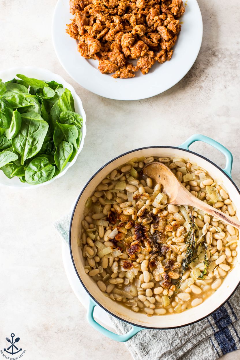 Overhead photo of a skillet filled with beans and spices, a bowl of spinach leaves and a plate of cooked chorizo sausage