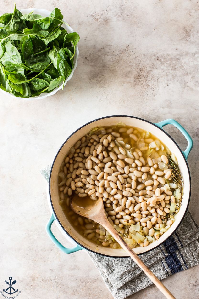 Overhead photo of a skillet of white beans and a bowl of spinach leaves