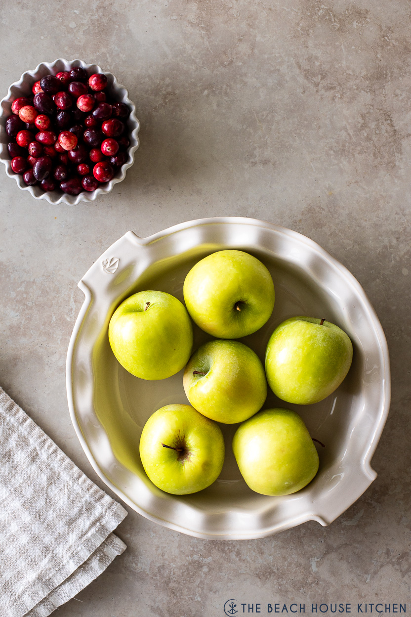 Overhead photo of a bowl of cranberries and a pie plate filled with Granny Smith apples
