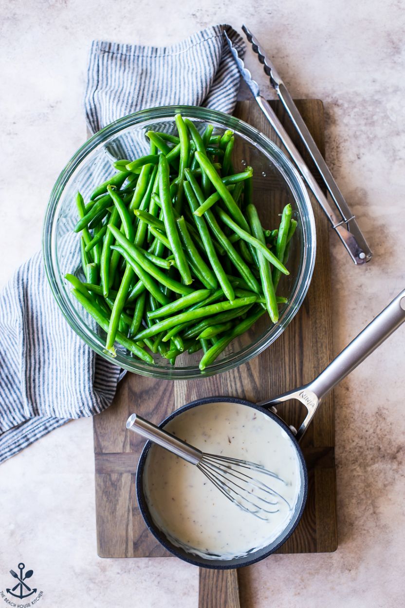 Overhead photo of a bowl of green beans and a small pot of Mornay sauce